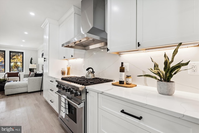 kitchen featuring wall chimney range hood, crown molding, high end stainless steel range, white cabinets, and light wood-type flooring