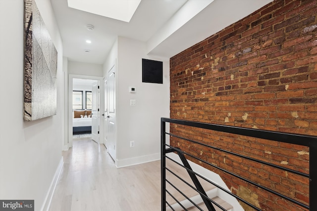 hall with light wood-type flooring and brick wall