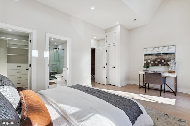 bedroom with a spacious closet, a closet, light wood-type flooring, and ensuite bath