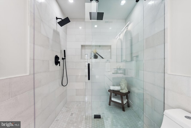 bathroom featuring toilet, a shower with door, and tile walls