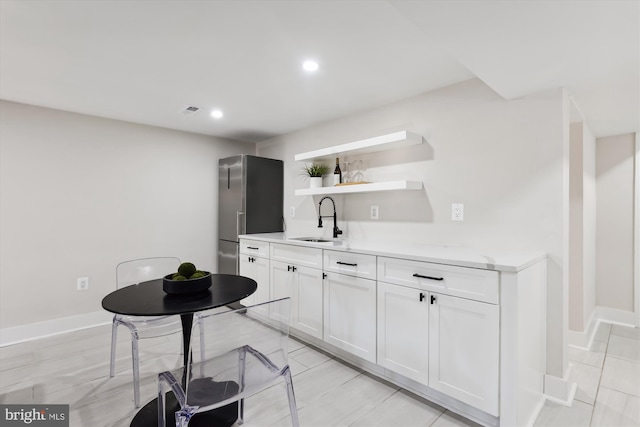 kitchen with white cabinetry, sink, and stainless steel refrigerator