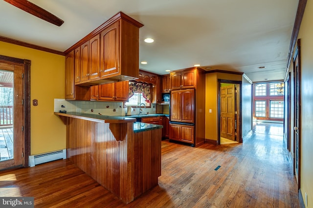 kitchen with kitchen peninsula, a healthy amount of sunlight, light hardwood / wood-style flooring, and a baseboard heating unit