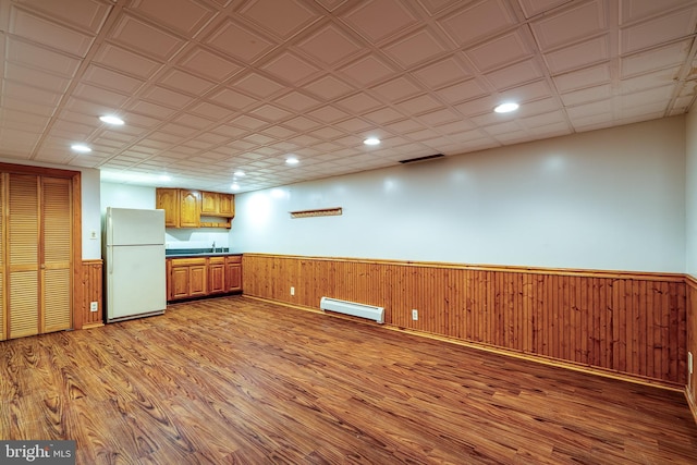 kitchen featuring sink, a baseboard radiator, light hardwood / wood-style flooring, white refrigerator, and wood walls