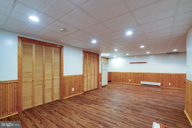 basement featuring hardwood / wood-style floors, white refrigerator, a baseboard heating unit, and wood walls