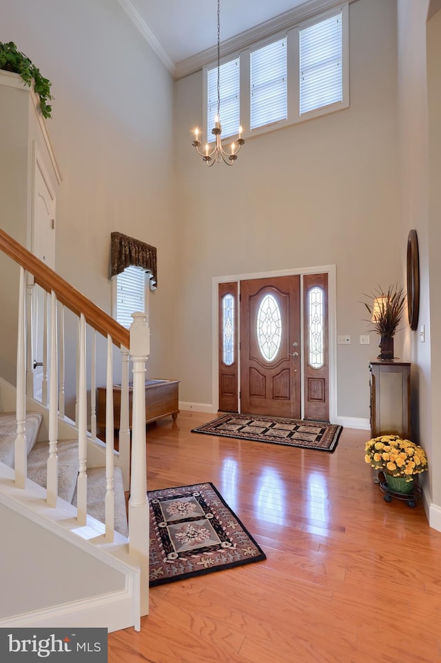 entryway featuring wood-type flooring, a notable chandelier, crown molding, and a high ceiling