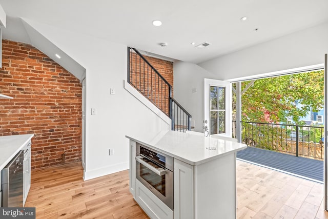 kitchen featuring stainless steel oven, beverage cooler, light wood-type flooring, a kitchen island, and brick wall