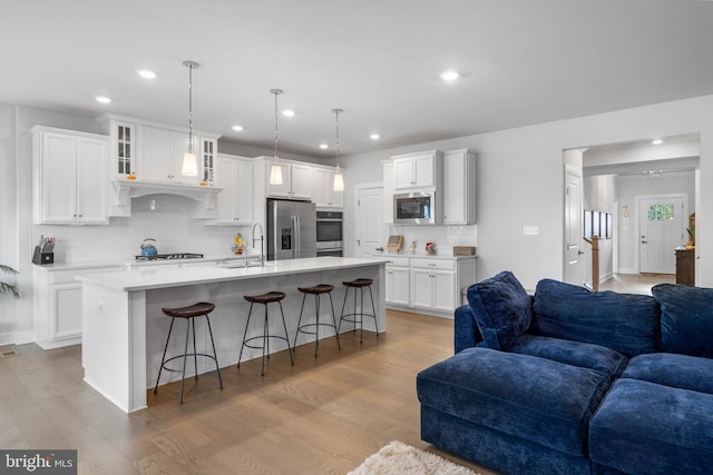 kitchen featuring appliances with stainless steel finishes, light wood-type flooring, white cabinetry, and an island with sink