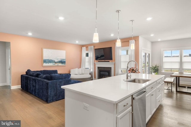 kitchen with stainless steel dishwasher, a kitchen island with sink, sink, white cabinets, and light hardwood / wood-style floors