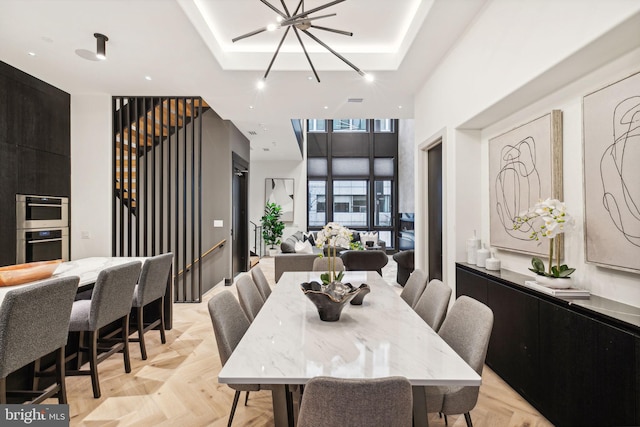 dining area featuring a chandelier, light parquet flooring, and a raised ceiling