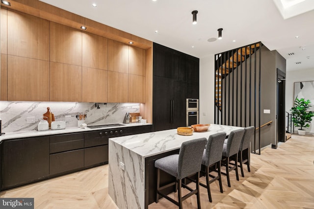 kitchen featuring decorative backsplash, light parquet flooring, light stone counters, and a kitchen island