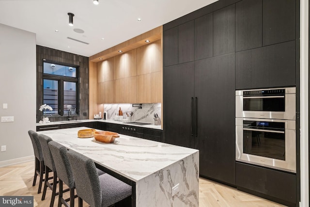 kitchen featuring light stone countertops, a center island, sink, double oven, and backsplash