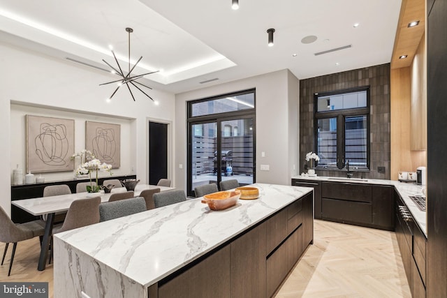 kitchen with a center island, sink, a notable chandelier, light parquet floors, and a tray ceiling