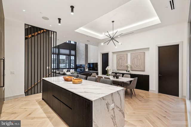 kitchen with a tray ceiling, light parquet floors, a spacious island, and a notable chandelier