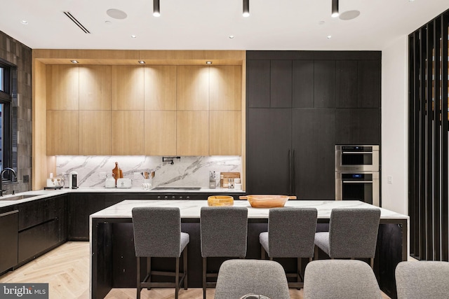 kitchen with a kitchen breakfast bar, backsplash, sink, light parquet flooring, and a kitchen island