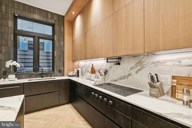 kitchen with gas stovetop, light stone countertops, sink, and light parquet flooring