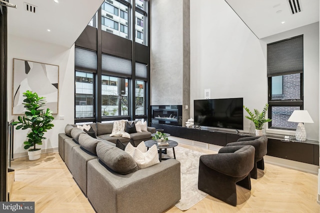 living room with a large fireplace, a high ceiling, and light parquet flooring