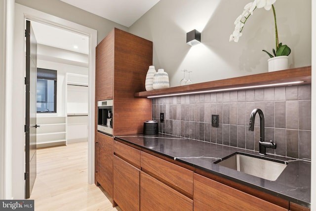 kitchen with tasteful backsplash, dark stone countertops, light hardwood / wood-style flooring, and sink