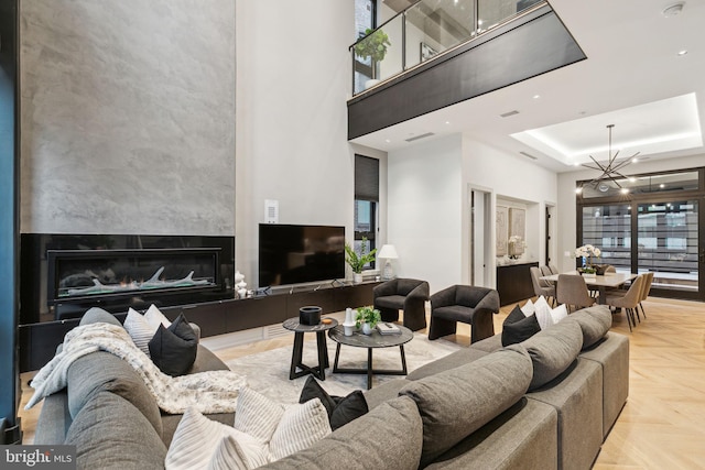 living room featuring a high ceiling, light parquet floors, a raised ceiling, a fireplace, and a chandelier