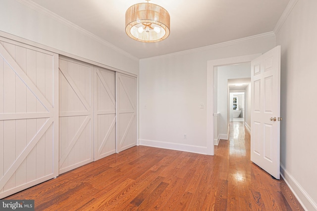 unfurnished bedroom featuring a chandelier, hardwood / wood-style flooring, a closet, and crown molding