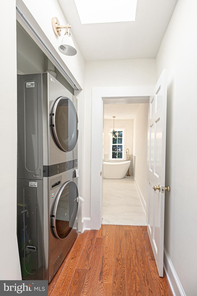 laundry area with a skylight, wood-type flooring, and stacked washer and clothes dryer