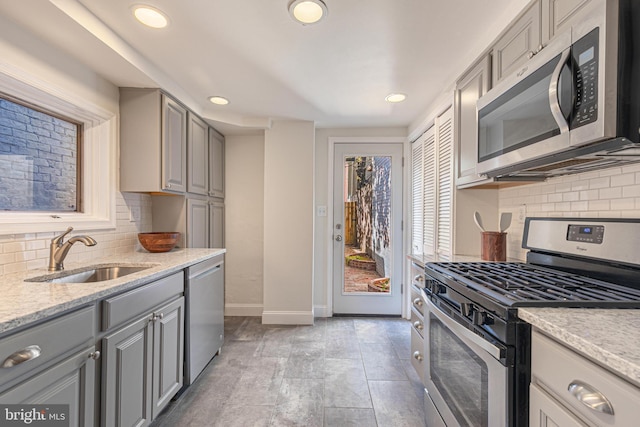 kitchen featuring backsplash, light stone counters, stainless steel appliances, sink, and gray cabinets