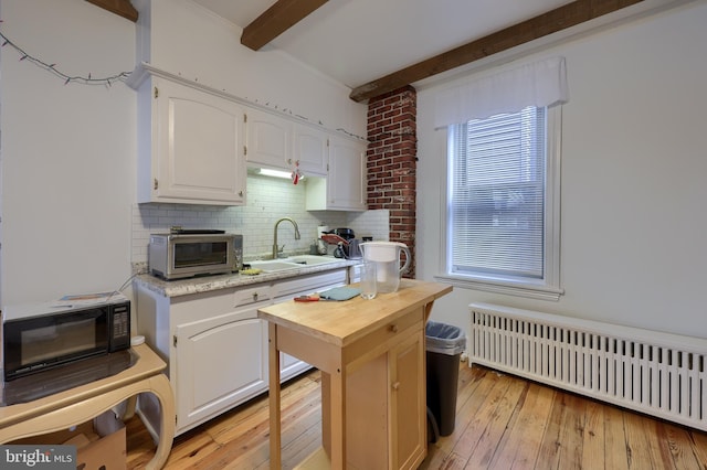 kitchen featuring light hardwood / wood-style floors, beam ceiling, white cabinets, and radiator heating unit