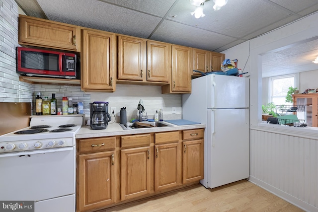 kitchen with light wood-type flooring, a paneled ceiling, white appliances, sink, and wood walls