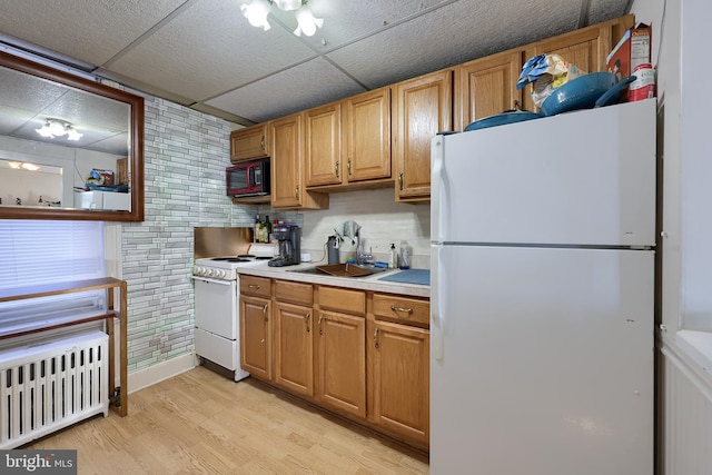 kitchen featuring radiator, sink, light hardwood / wood-style floors, white appliances, and a paneled ceiling