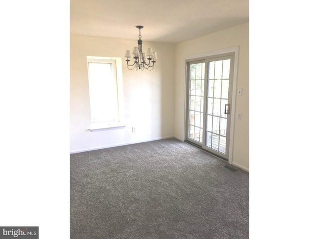 empty room featuring dark carpet and an inviting chandelier