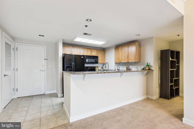 kitchen featuring light carpet, kitchen peninsula, a breakfast bar, black appliances, and stone countertops