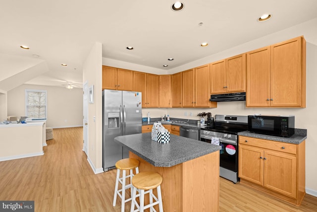 kitchen featuring ceiling fan, a kitchen breakfast bar, appliances with stainless steel finishes, a kitchen island, and light wood-type flooring