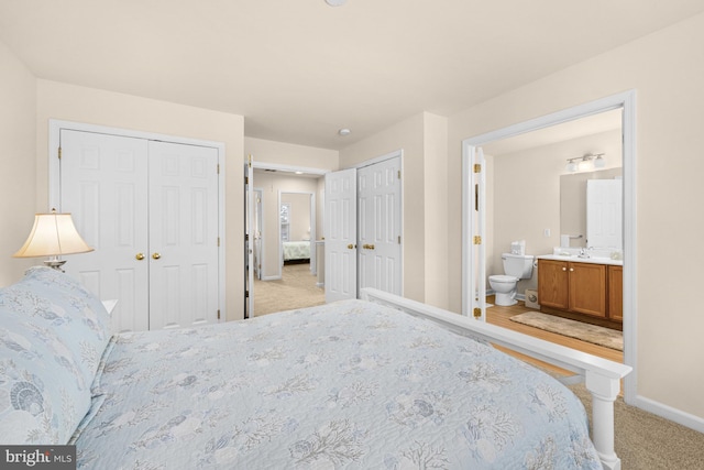 bedroom with ensuite bath, multiple closets, sink, and light colored carpet