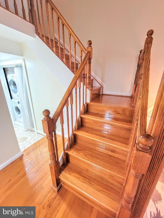 stairway with hardwood / wood-style floors and stacked washer / drying machine