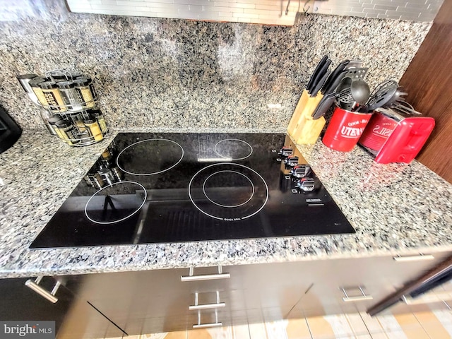 interior details featuring black electric stovetop, light stone counters, and backsplash