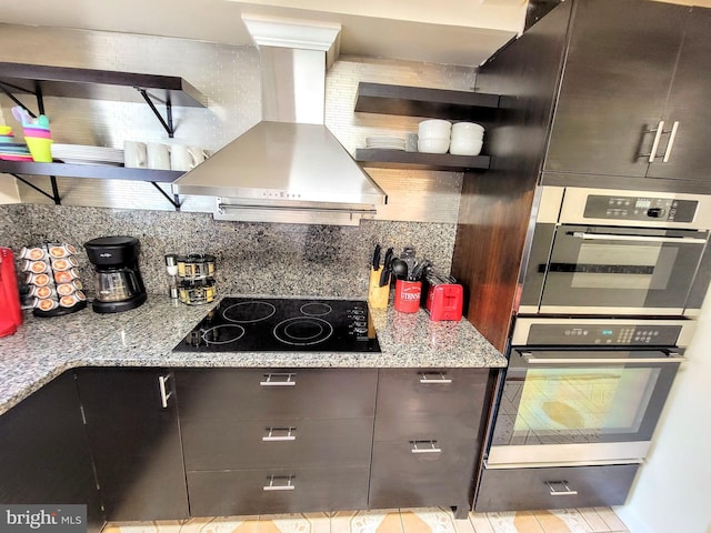 kitchen featuring black electric cooktop, light stone countertops, dark brown cabinets, and wall chimney exhaust hood