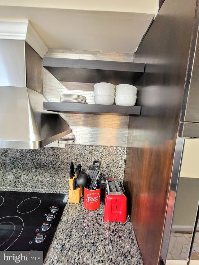 kitchen featuring backsplash, black cooktop, wall chimney exhaust hood, and light stone counters