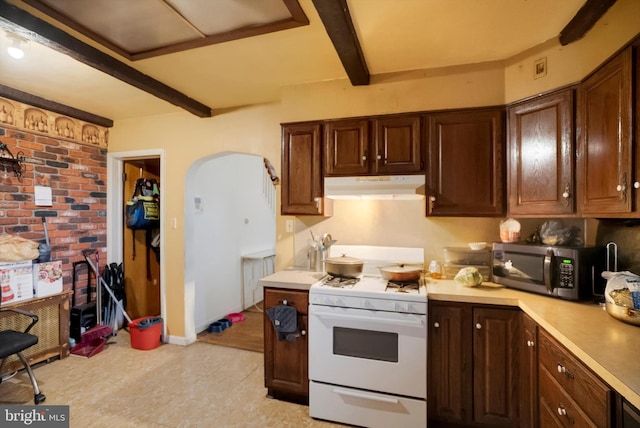 kitchen featuring beam ceiling, dark brown cabinets, white range with gas stovetop, and brick wall