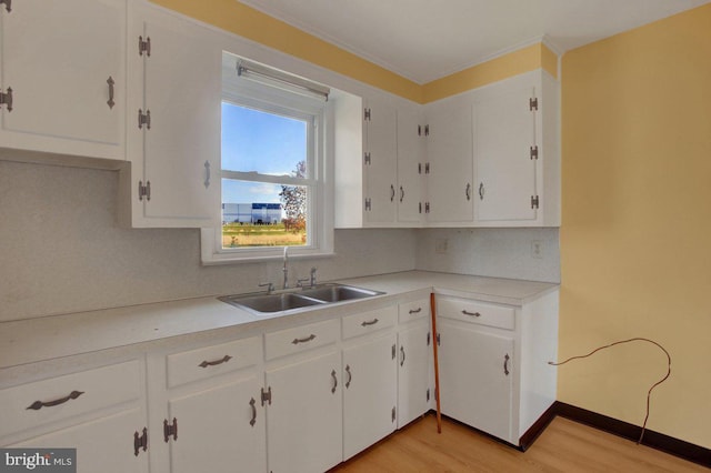 kitchen with tasteful backsplash, ornamental molding, sink, light hardwood / wood-style flooring, and white cabinets