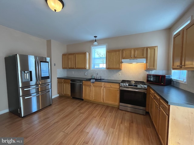 kitchen with hanging light fixtures, sink, appliances with stainless steel finishes, tasteful backsplash, and light hardwood / wood-style floors