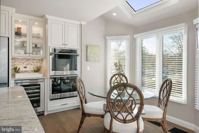 dining room with dark hardwood / wood-style floors, lofted ceiling with skylight, and beverage cooler