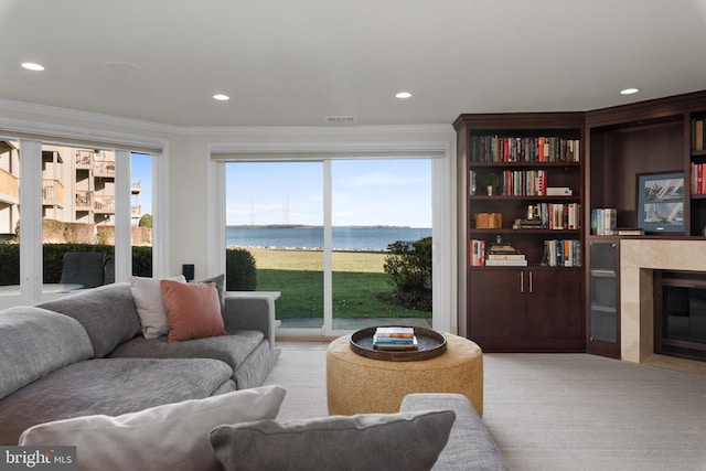 carpeted living room with a water view, ornamental molding, and a fireplace