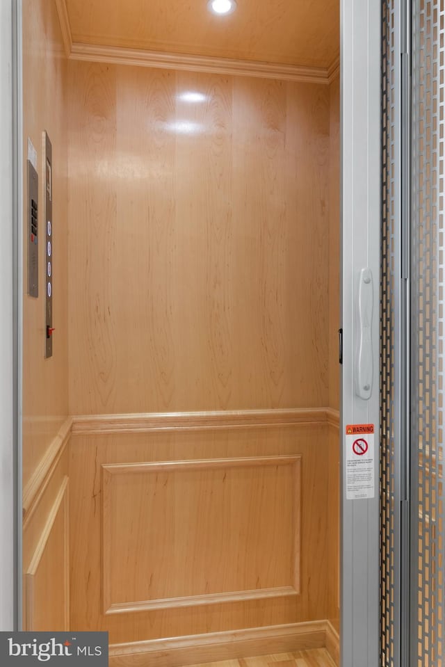 room details featuring ornamental molding, elevator, wooden walls, and hardwood / wood-style floors