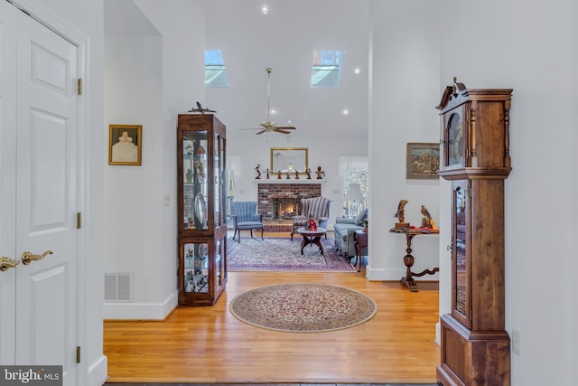 foyer with a high ceiling, a skylight, hardwood / wood-style flooring, ceiling fan, and a fireplace