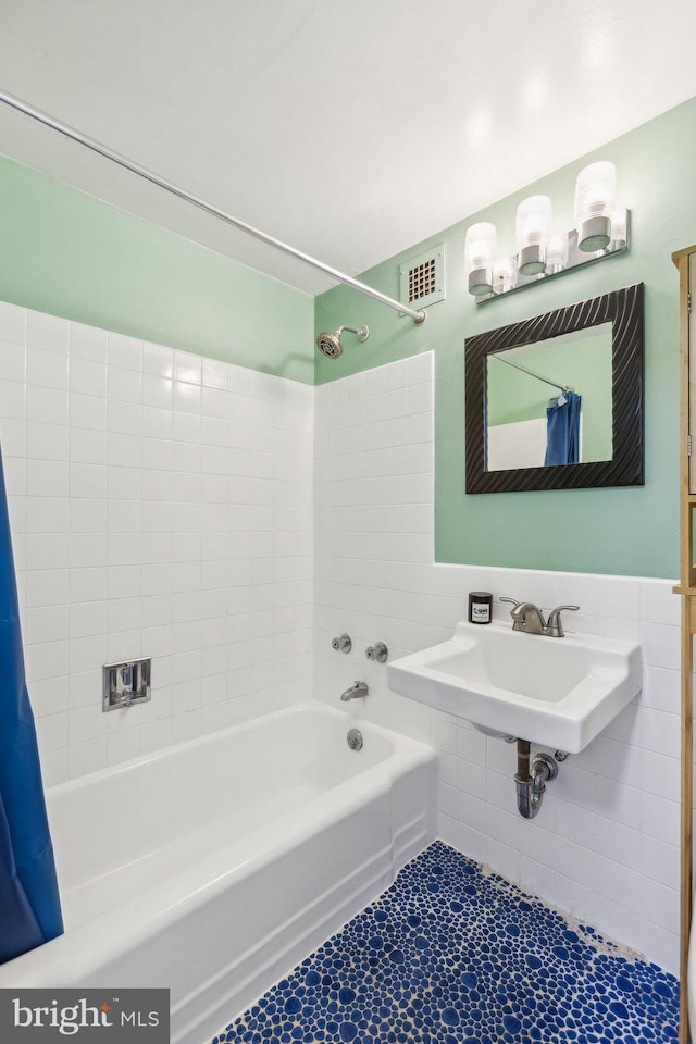 bathroom featuring tile patterned floors, shower / bath combination with curtain, sink, and tile walls