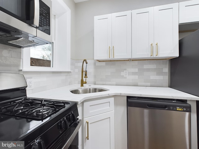 kitchen with white cabinets, appliances with stainless steel finishes, light stone counters, and sink