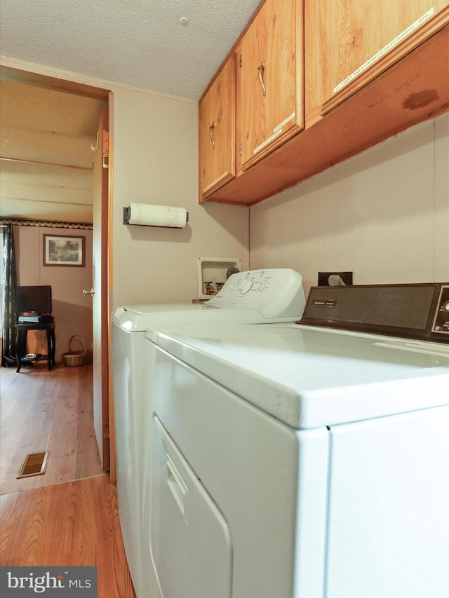 washroom with washer and clothes dryer, cabinets, a textured ceiling, and light hardwood / wood-style flooring