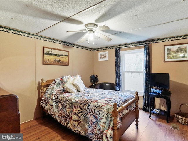 bedroom featuring ceiling fan, hardwood / wood-style floors, and a textured ceiling