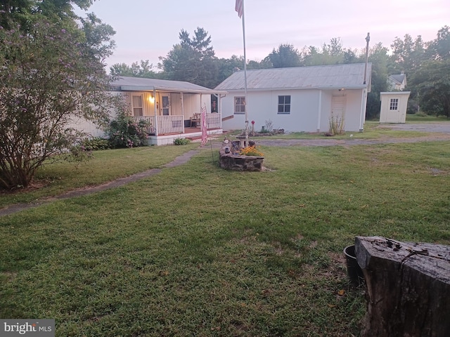 back house at dusk featuring a porch, a yard, and a storage shed