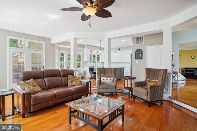 living room featuring light wood-style flooring, visible vents, and ceiling fan