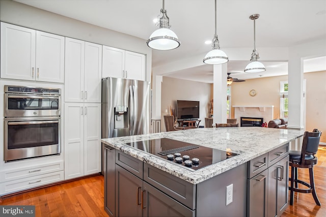 kitchen featuring light wood finished floors, a glass covered fireplace, light stone counters, stainless steel appliances, and a kitchen bar